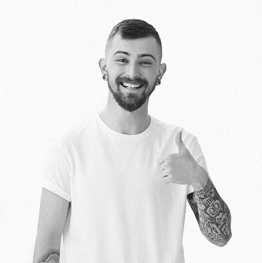 Smiling man giving a thumbs-up gesture with tattoos on his arm.