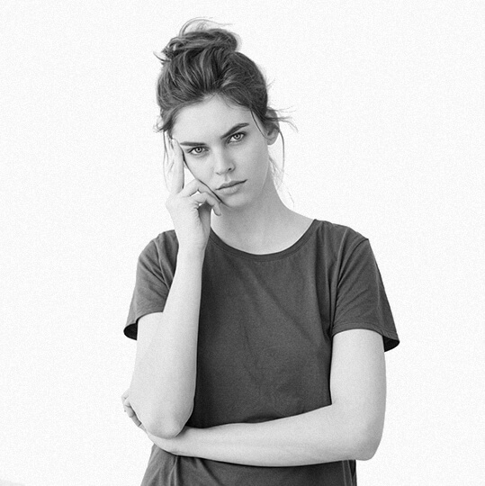 Black and white portrait of a thoughtful young woman with hair tied up, wearing a plain t-shirt.