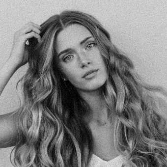 Black and white portrait of a woman with long wavy hair touching her head.