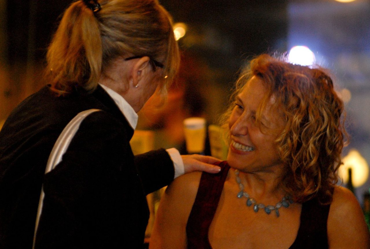 Two women engaged in a warm conversation at a cozy evening gathering.