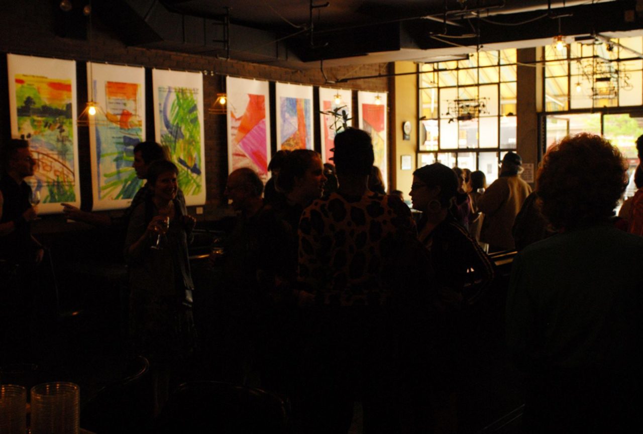 Dimly lit room with people socializing and colorful posters on the wall.